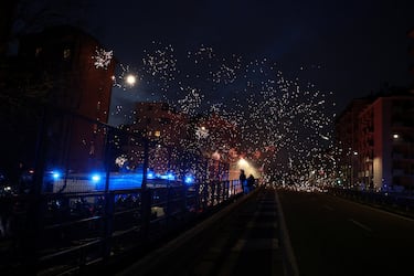Agentes de policía se sitúan detrás de vehículos, mientras los fuegos artificiales explotan mientras los manifestantes los utilizan contra las fuerzas del orden al intentar bloquear una carretera que conduce al Santa Giulia Arena, el día de una protesta contra el impacto ambiental, económico y social de los Juegos Olímpicos de Invierno Milano-Cortina 2026.