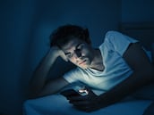 Addicted man chatting and surfing on the Internet with smart phone late at night in bed. Bored, sleepless and tired in dark room with moody light. In insomnia and mobile addiction concept.