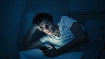 Addicted man chatting and surfing on the Internet with smart phone late at night in bed. Bored, sleepless and tired in dark room with moody light. In insomnia and mobile addiction concept.