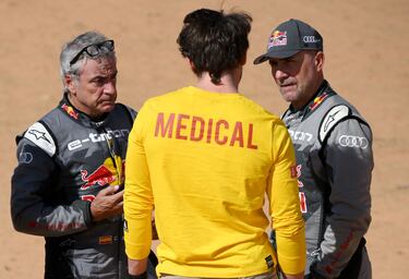 Los pilotos de Audi Stephane Peterhansel  y Carlos Sainz hablan con un miembro del personal médico después de sus respectivos accidente durante la Etapa 6 del Dakar 2023.