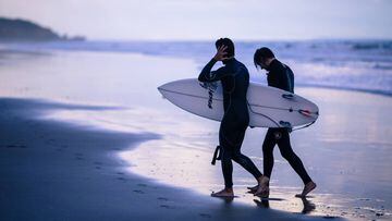 Dos hombres con traje de neopreno para el surf salen del agua.