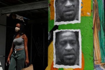A woman walks with a protective face covering past a mural of George Floyd, along 125th street in the Harlem neighbourhood of New York City, New York, U.S., 9 July 2020.