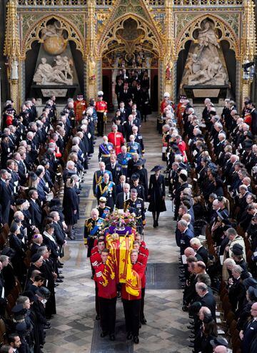 El rey Carlos III, la reina consorte, la princesa real, el vicealmirante Sir Tim Laurence, el duque de York, el conde de Wessex, la condesa de Wessex, el príncipe de Gales, la princesa de Gales, el príncipe George, la princesa Charlotte, el El duque de Sussex, la duquesa de Sussex, Peter Phillips y el conde de Snowdon siguen detrás del ataúd de la reina Isabel II, envuelto en el estandarte real con la corona del estado imperial y el orbe y el cetro del soberano, mientras se saca de la Abadía de Westminster.