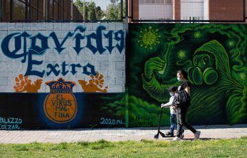A woman and a boy wearing face masks walk past a COVID-19 graffiti in Barcelona on April 26, 2020 amid a national lockdown to prevent the spread of the coronavirus.